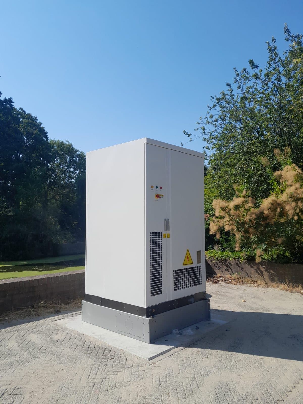 One battery cabinet on a concrete pad, among trees