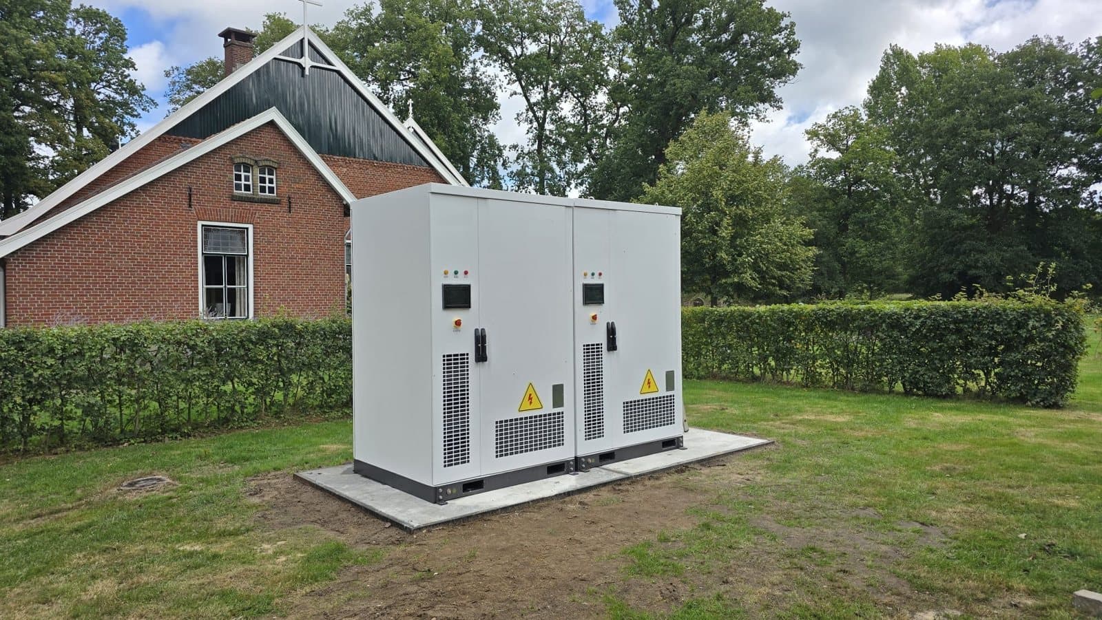Two battery cabinets on a concrete pad on the lawn next to a farmhouse